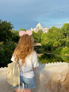 a woman with long hair wearing a mouse ears headband looking out over a pond