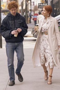 a man and woman are walking down the street holding coffee in their hands while looking at each other