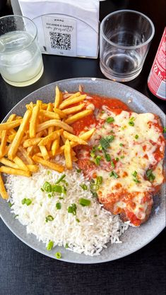 a plate with rice, french fries and meat covered in sauce on it next to a glass of water