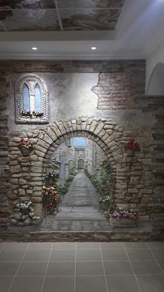 a stone wall with an archway and flowers on the side, in front of a tiled floor