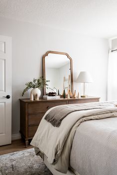 a bedroom with a bed, dresser and mirror on it's side table in front of a white door