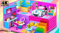 a hand holding up a toy house with furniture and accessories on the inside, in front of a multi - colored background