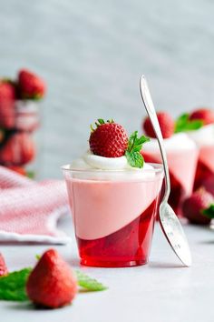 two cups filled with ice cream and strawberries on top of each other next to spoons