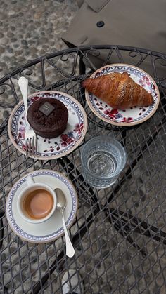 two plates with pastries and coffee on a metal table outdoors in the sun,