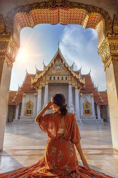 a woman sitting on the ground in front of a building with columns and arches, looking up into the sky