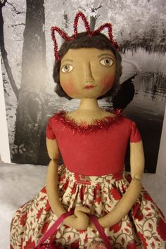 the doll is wearing a red dress and holding a pink purse with a black bird on it