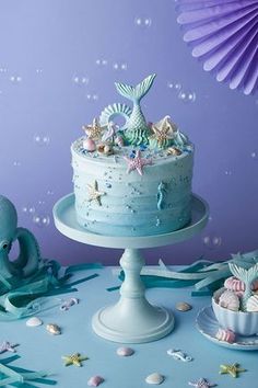 an image of a blue cake with mermaid decorations on it and under the sea waves