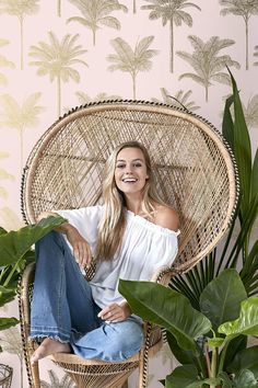 a woman sitting in a wicker chair with palm trees on the wall behind her