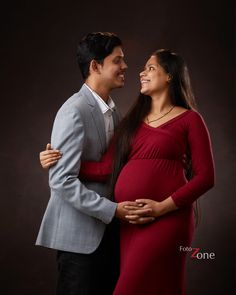 a pregnant woman in a red dress standing next to a man wearing a gray suit