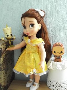 a doll with long hair standing next to a toy cat and other toys on a table