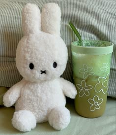 a white stuffed rabbit sitting next to a cup with a drink in it's mouth