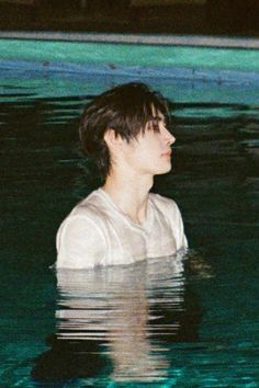 a man standing in the water wearing a white shirt and looking off into the distance