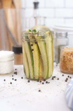 a jar filled with cucumbers sitting on top of a counter next to spices