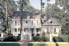 a large white house surrounded by trees and bushes in the front yard with a brick walkway leading to it