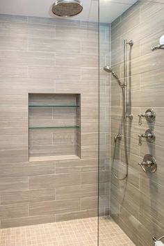 a walk in shower sitting next to a glass door and tiled walls with shelves on each side