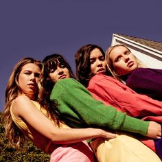 four young women are standing together in front of a house and one is looking up at the sky