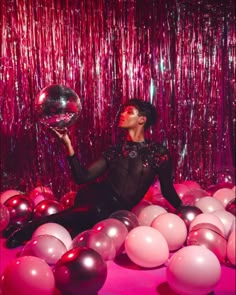 a woman sitting on the ground surrounded by balloons and streamers holding a disco ball