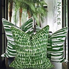 two green and white pillows sitting on top of a table next to a palm tree