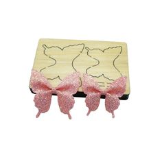 two pink bows are on top of a wooden box with glittered ears and tails