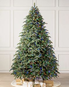 a christmas tree with presents under it on a wooden floor in front of a white wall