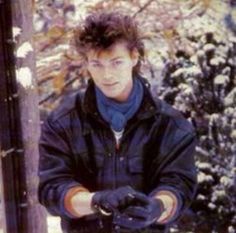 a young man in black jacket and gloves standing next to snow covered trees with one hand on his hip