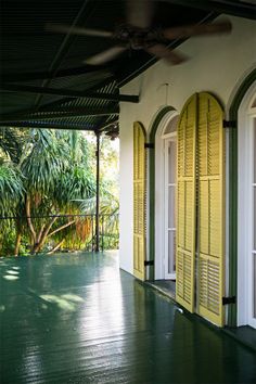 an empty porch with yellow shutters and palm trees