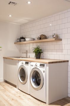 a washer and dryer in a room with white tile walls, wooden flooring and shelves on the wall