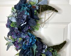 a wreath with blue flowers and greenery hanging on the front door to welcome guests