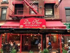 the outside of a restaurant with red awnings and people sitting at tables in front