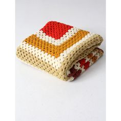 a crocheted blanket with red, yellow and white squares on it sitting on top of a table