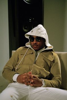 a man sitting on top of a couch wearing a white hat and jacket with his hands in his pockets