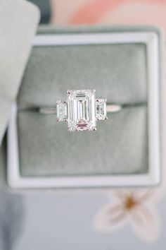 an emerald - cut diamond ring sits in a box on top of a flowery surface