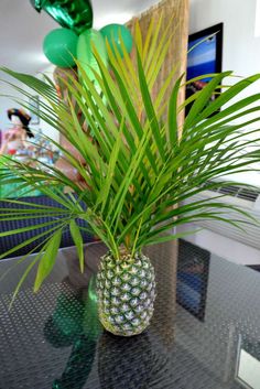 a pineapple plant sitting on top of a glass table with balloons in the background