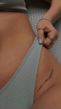 a woman is showing off her tiny tattoo on her lower back and the bottom part of her stomach