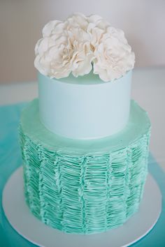 a green and white cake with flowers on top is sitting on a blue tablecloth