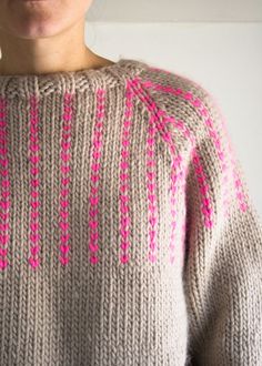 a woman wearing a sweater with pink and grey designs on the side, standing in front of a white wall