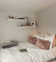 a bed with white sheets and pink pillows in a bedroom next to a laptop computer