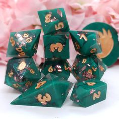 green and gold dice set with numbers on each side, in front of pink flowers