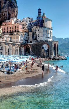 people are on the beach in front of some buildings and umbrellas near the water