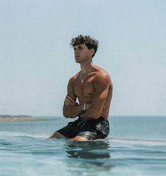 a shirtless man sitting on top of a surfboard in the middle of the ocean