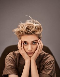 a woman sitting in a chair with her hands on her face and looking at the camera