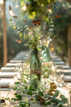 the table is set with glass vases and bottles filled with flowers, greenery and butterflies