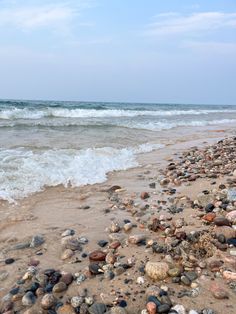 the beach is littered with rocks and pebbles as waves crash in the water behind it