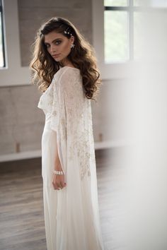 a woman in a long white dress standing on a wooden floor with her arms behind her back