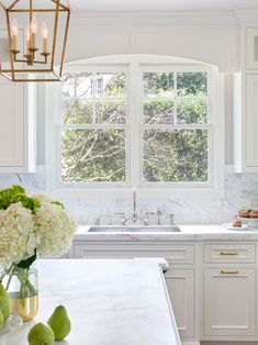 a kitchen with white cabinets and marble counter tops, an island in front of the window