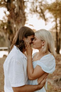 a man and woman standing next to each other in front of trees with leaves on the ground