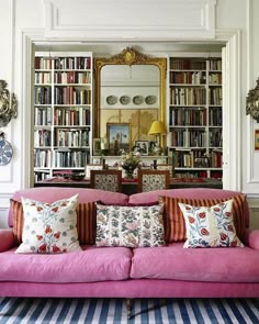 a living room with pink couches and bookshelves in front of a mirror