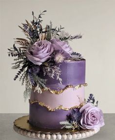 there is a purple cake with flowers on the top and gold trim around the edges