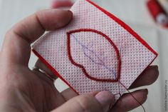 a hand holding a piece of fabric with a red thread on it and a heart