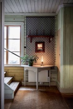 a room with a table, stairs and potted plant in the corner next to a window